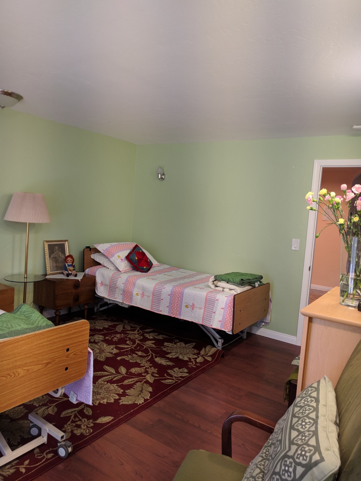 A cozy bedroom with a hospital bed, floral decorations, and soft lighting.