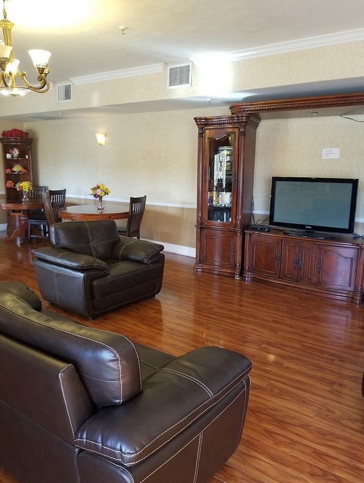 A cozy living room with leather chairs, a large television, and a dining area in the background.