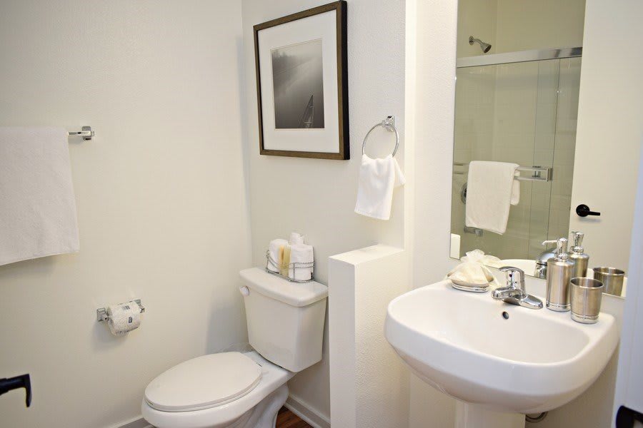 A minimalist bathroom featuring a toilet and a pedestal sink with a towel rack and framed artwork on the wall.
