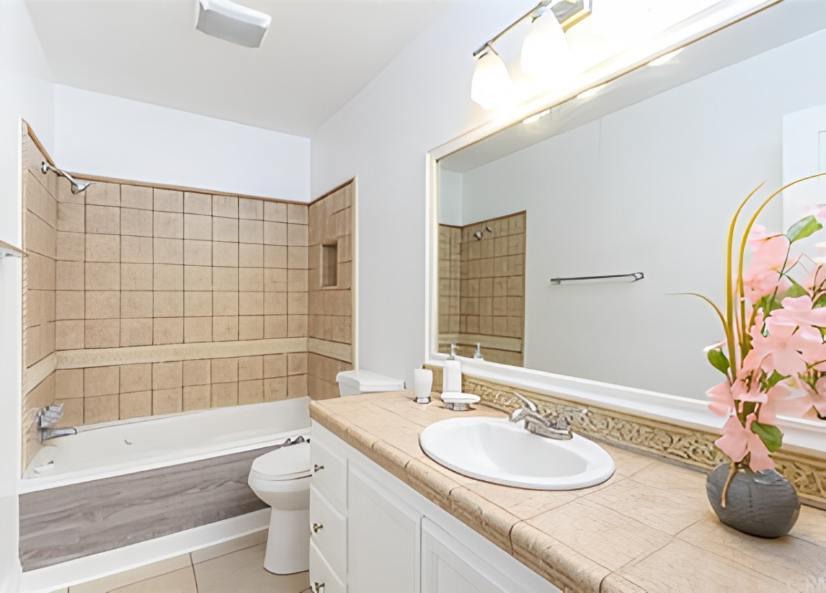 A modern bathroom with a tiled bathtub, sink, and large mirror.