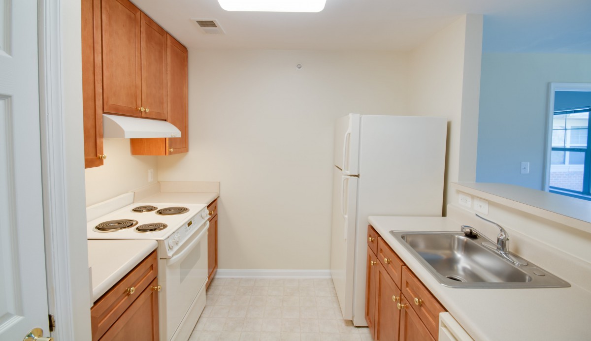 A compact apartment kitchen with wooden cabinets and white appliances.