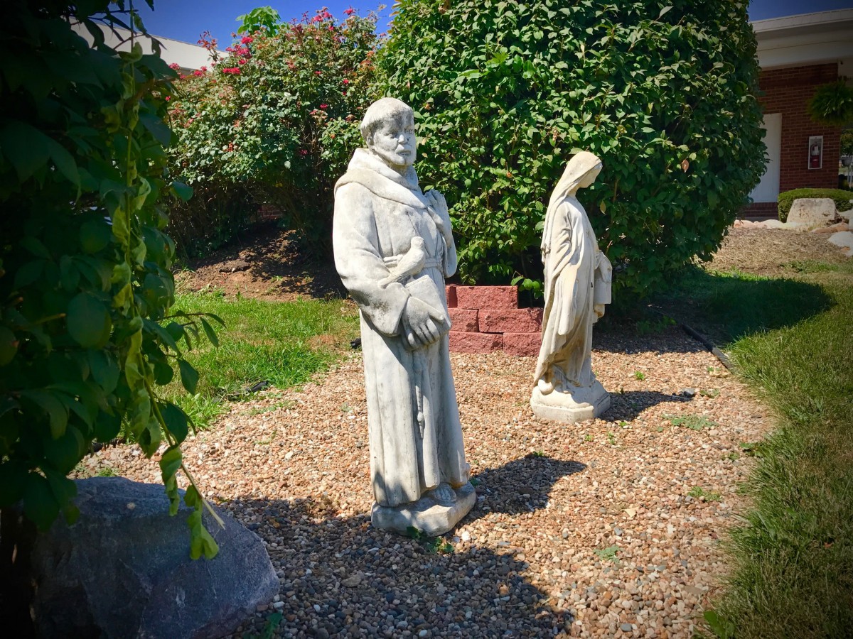 Two statues stand in a serene garden setting, surrounded by lush greenery.