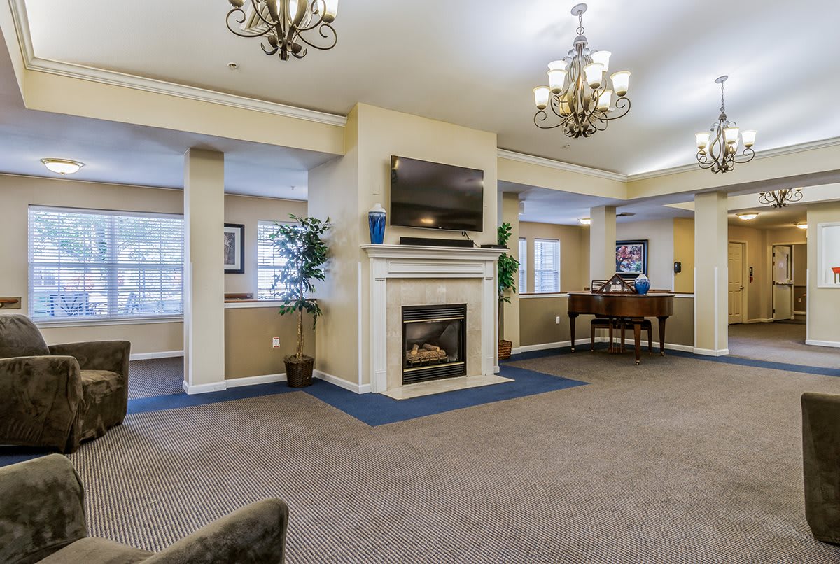 A cozy living room with a fireplace and a mounted television, featuring elegant chandeliers and a piano.