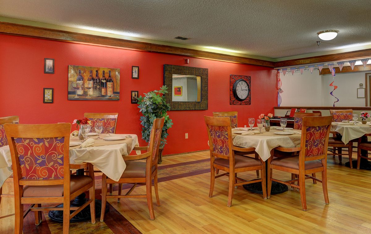A cozy restaurant dining area with red walls, elegantly set tables, and wooden chairs on a polished floor.