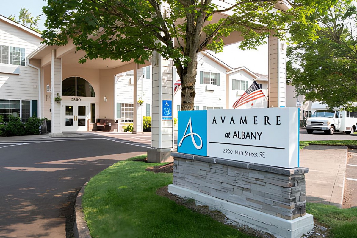 Entrance to Avamere at Albany with a sign and driveway surrounded by trees.