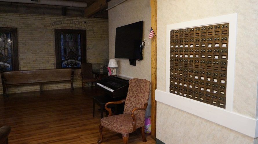 An interior room featuring a piano, armchair, wall-mounted TV, and a set of mailboxes.