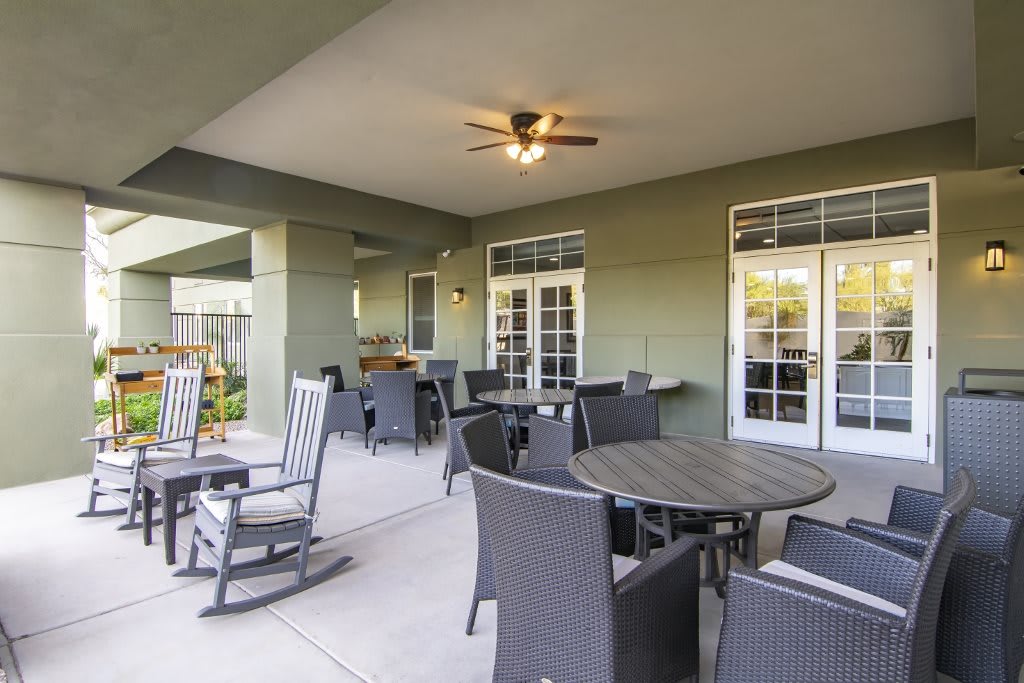 A cozy outdoor patio area with tables, chairs, and rocking chairs under a covered space.