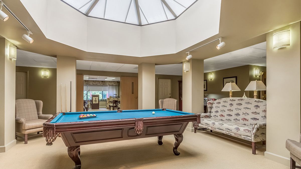 A recreation room featuring a billiard table under a large skylight, accompanied by a comfortable seating area.