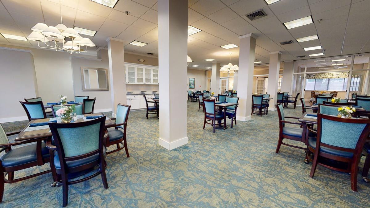 A spacious dining area with multiple tables and chairs, featuring a carpeted floor and overhead lighting.