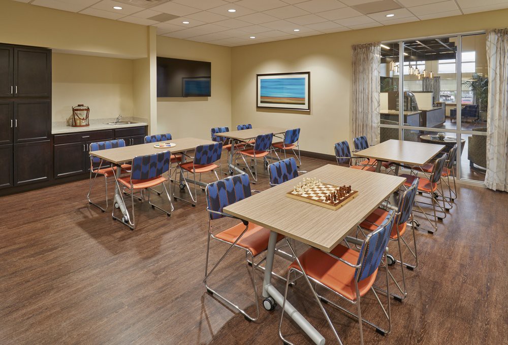 A modern conference room with tables, chairs, and a television on the wall.
