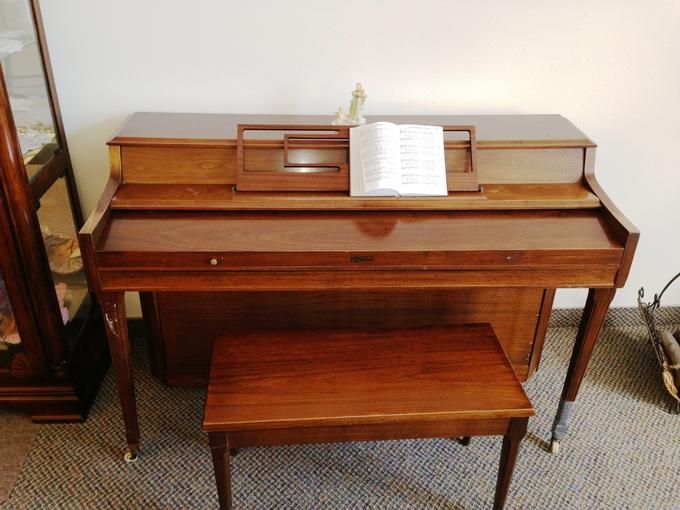 A wooden piano with a matching bench and an open music book on the stand.