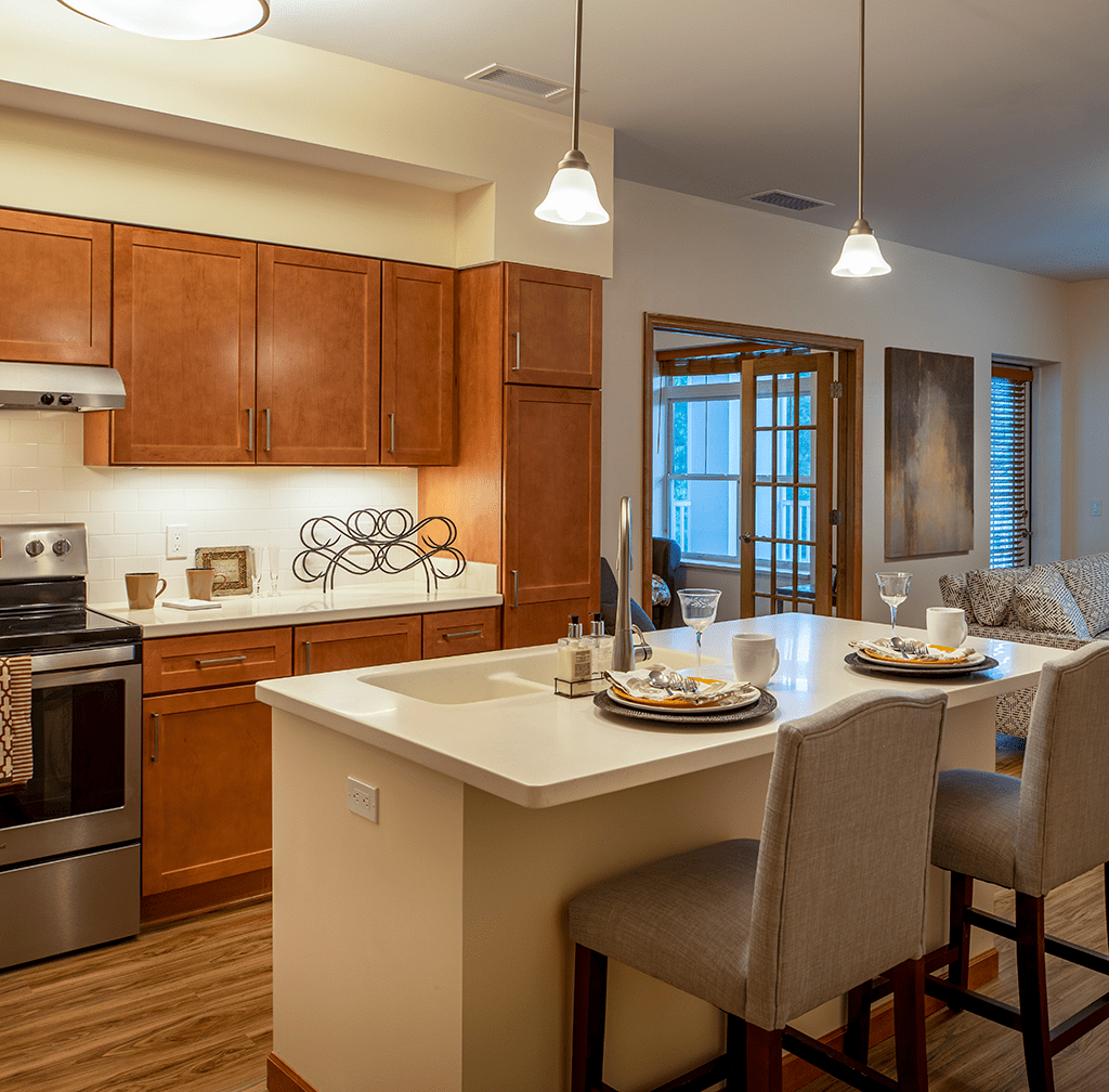A modern kitchen interior featuring a central island with bar stools and pendant lighting.