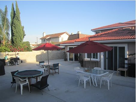 A spacious patio area with tables, chairs, and umbrellas in a residential backyard.
