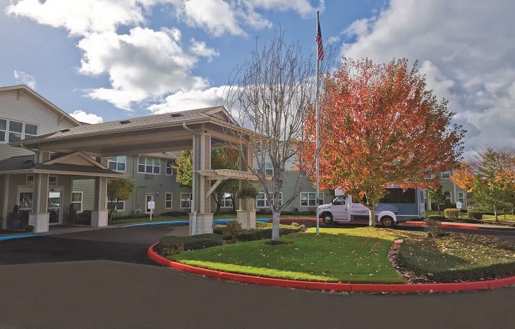 A building entrance with a circular driveway, surrounded by trees under a partly cloudy sky.