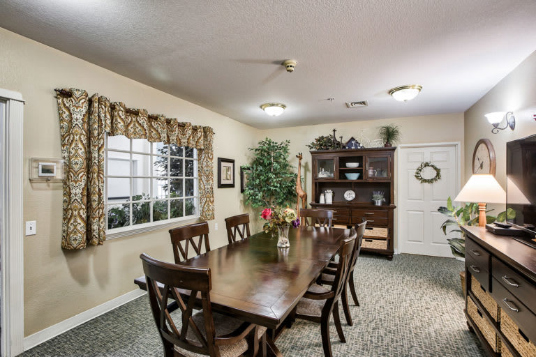 A well-furnished dining room with a long table, multiple chairs, and decorative elements like curtains and indoor plants.