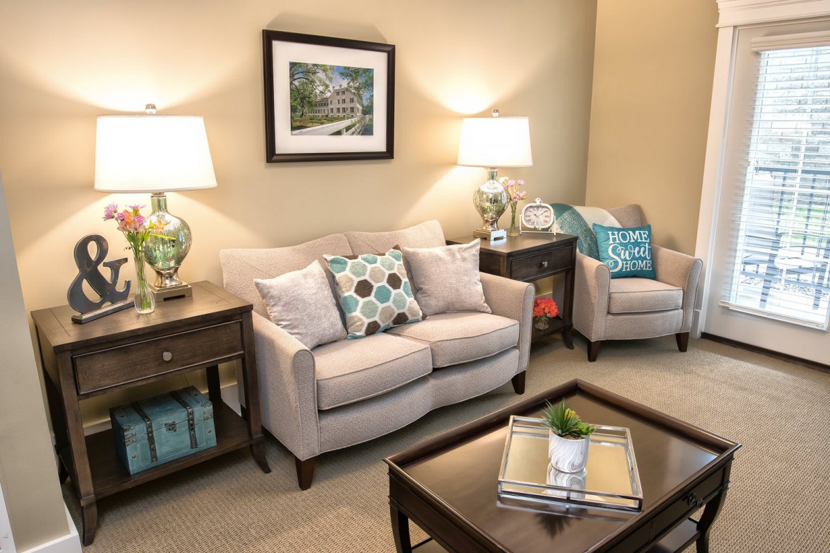 A cozy living room with a beige sofa and armchair, accented by colorful pillows and illuminated by matching table lamps.