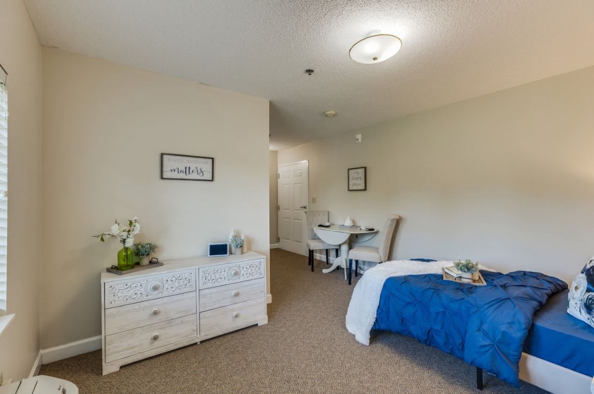 A cozy bedroom with a neatly made bed, dresser, and dining table set.
