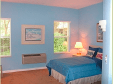 A cozy bedroom with blue walls, featuring a bed and a lamp by the window.