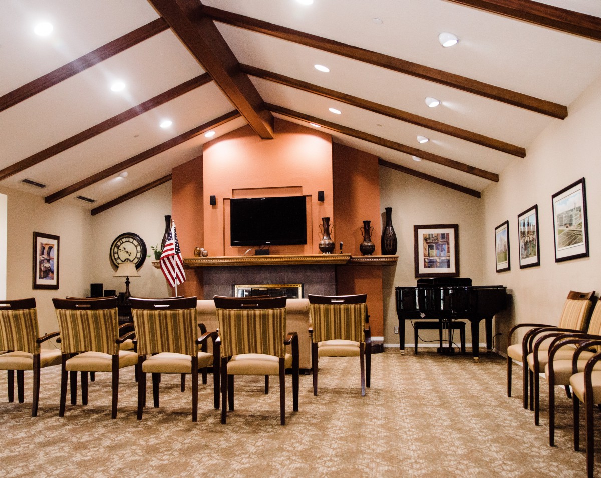 A spacious room with a beamed ceiling, featuring seating, a television, and a piano.