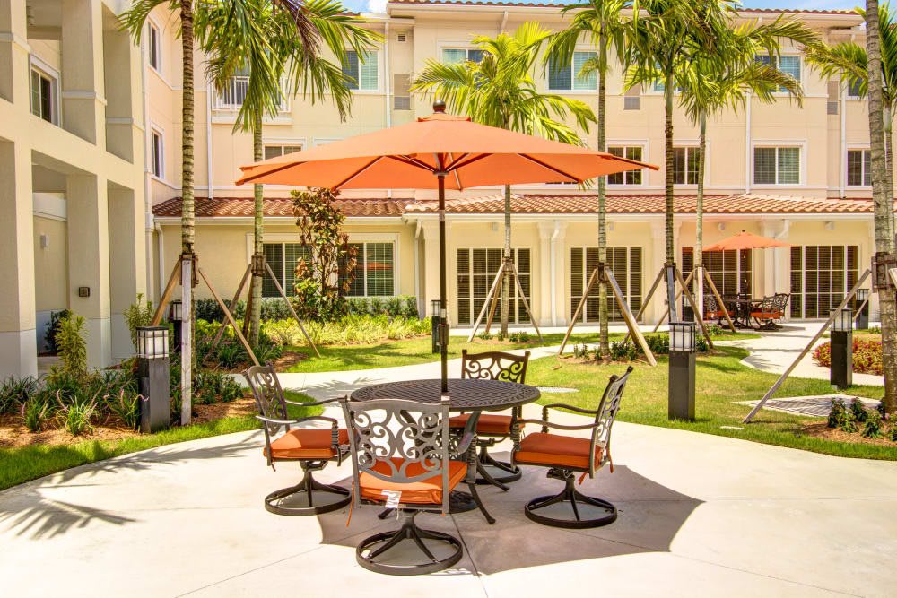 A sunny patio with an orange umbrella, surrounded by palm trees.