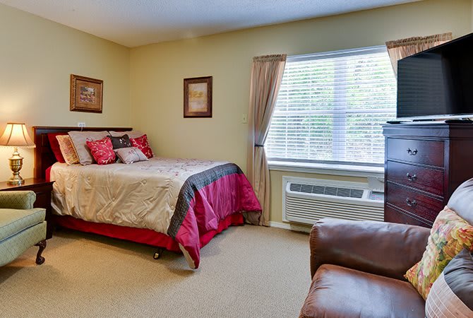 A cozy bedroom with a neatly made bed, window with curtains, and comfortable furnishings.
