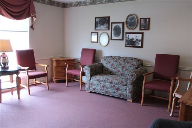 A vintage-style living room with a floral sofa, two chairs, and framed pictures on the wall.