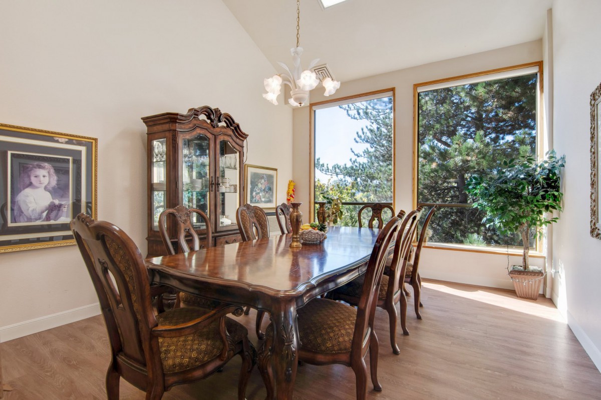 A spacious dining room with a wooden table, ornate chairs, and a chandelier, featuring large windows that allow natural light to fill the space.