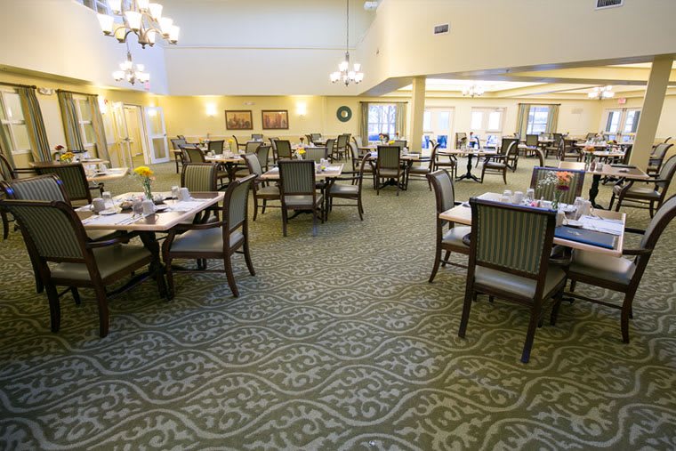 An elegant dining area with neatly arranged tables and chairs, featuring chandeliers and intricate carpet designs.
