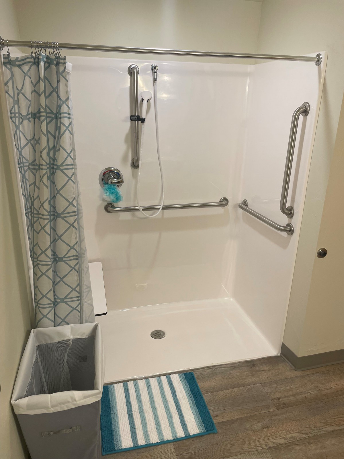 An accessible bathroom shower featuring grab bars and a patterned curtain.