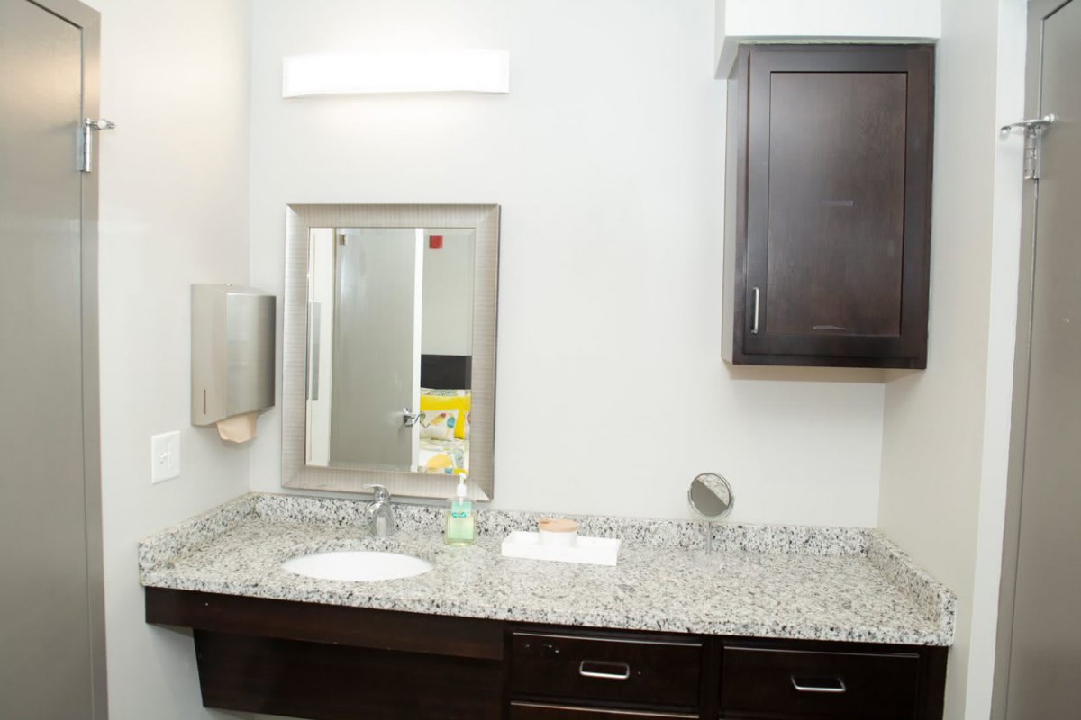 A clean and modern bathroom with a granite countertop, mirror, and storage cabinet.