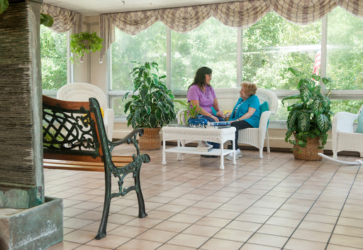 Two individuals engaged in a heartfelt conversation in a bright, plant-filled sitting area.