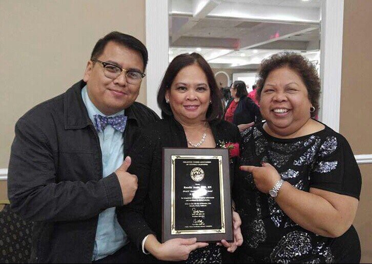 A group of three people smiling, one of whom is holding an award plaque at a celebration event.