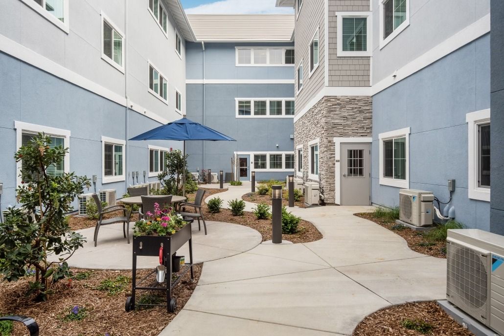 A courtyard featuring outdoor seating and landscaped pathways surrounded by a building with blue walls.