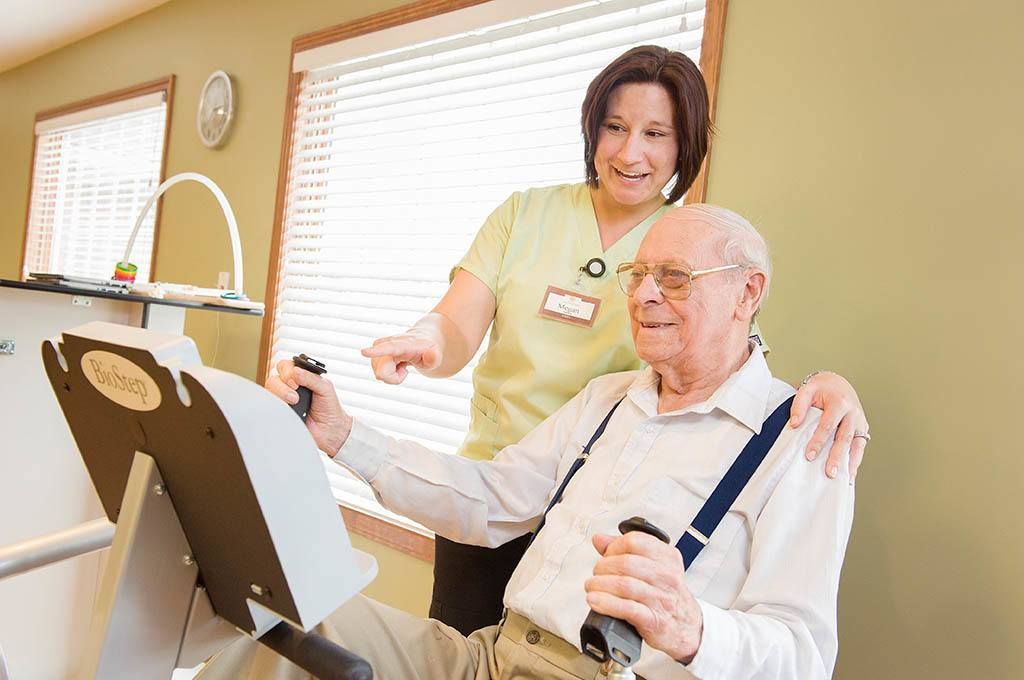 A nurse assists an elderly man during an exercise session in a healthcare facility.