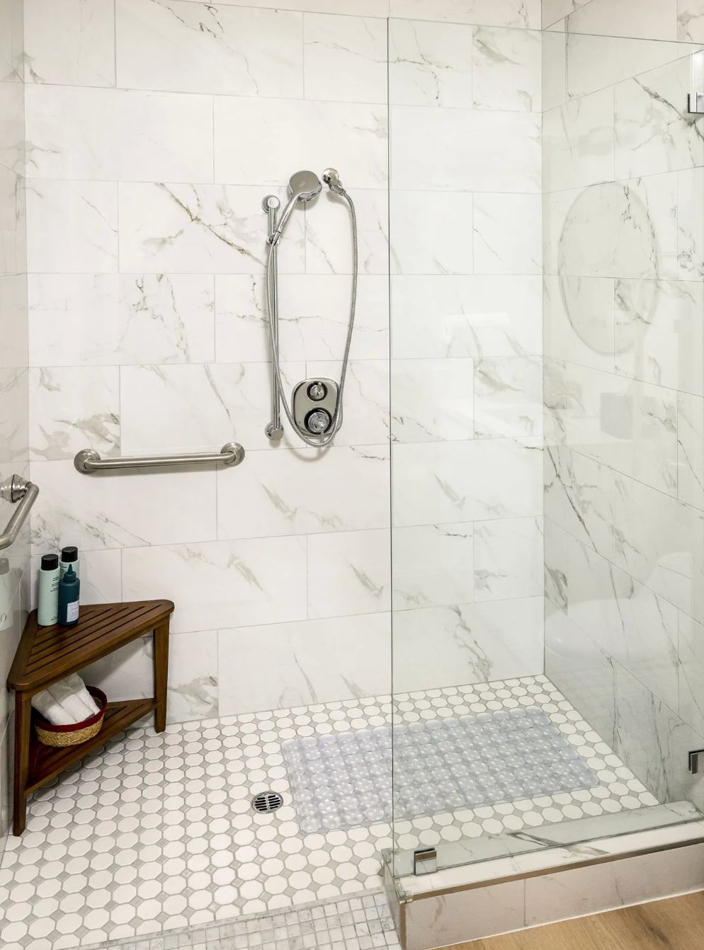 A modern shower with glass doors, marble tiles, and a small wooden bench.