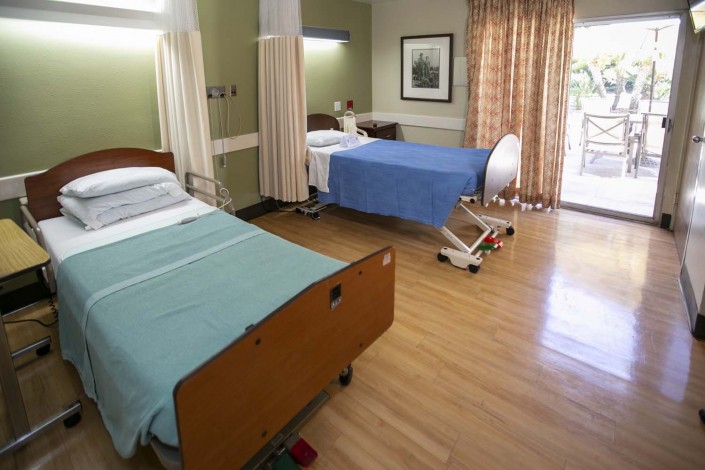 A well-lit hospital room with two beds and a wooden floor.