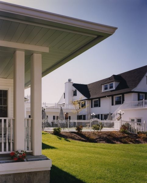 A charming white house featuring a spacious front porch and well-maintained landscaping.