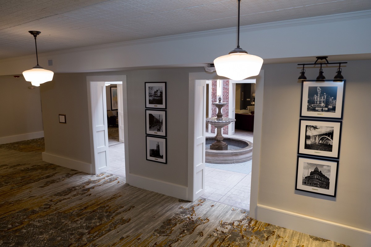 A hallway with framed photographs on the walls leads to a room featuring a fountain.