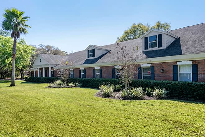 A large brick residential house with a well-maintained lawn and surrounding trees.