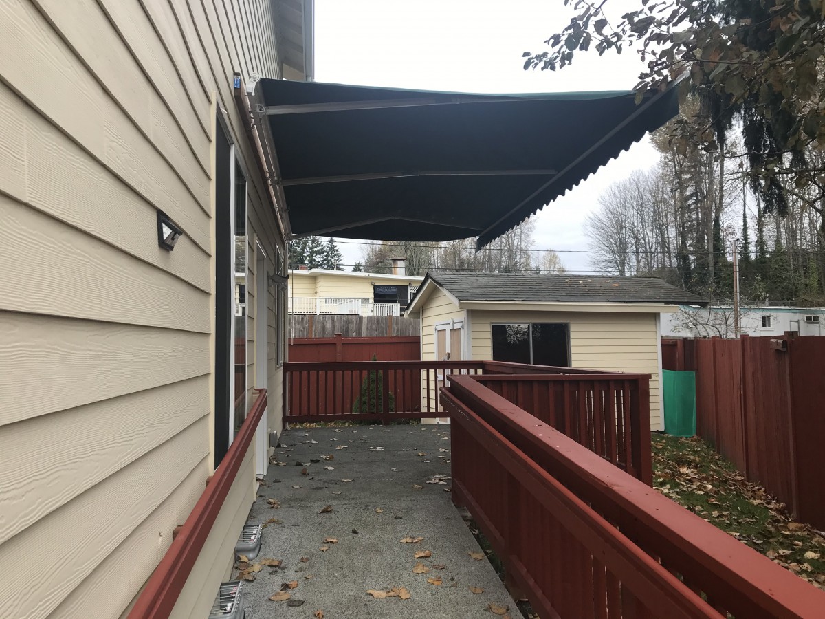 A house with a deck featuring an extended awning, surrounded by a red fence on an overcast day.