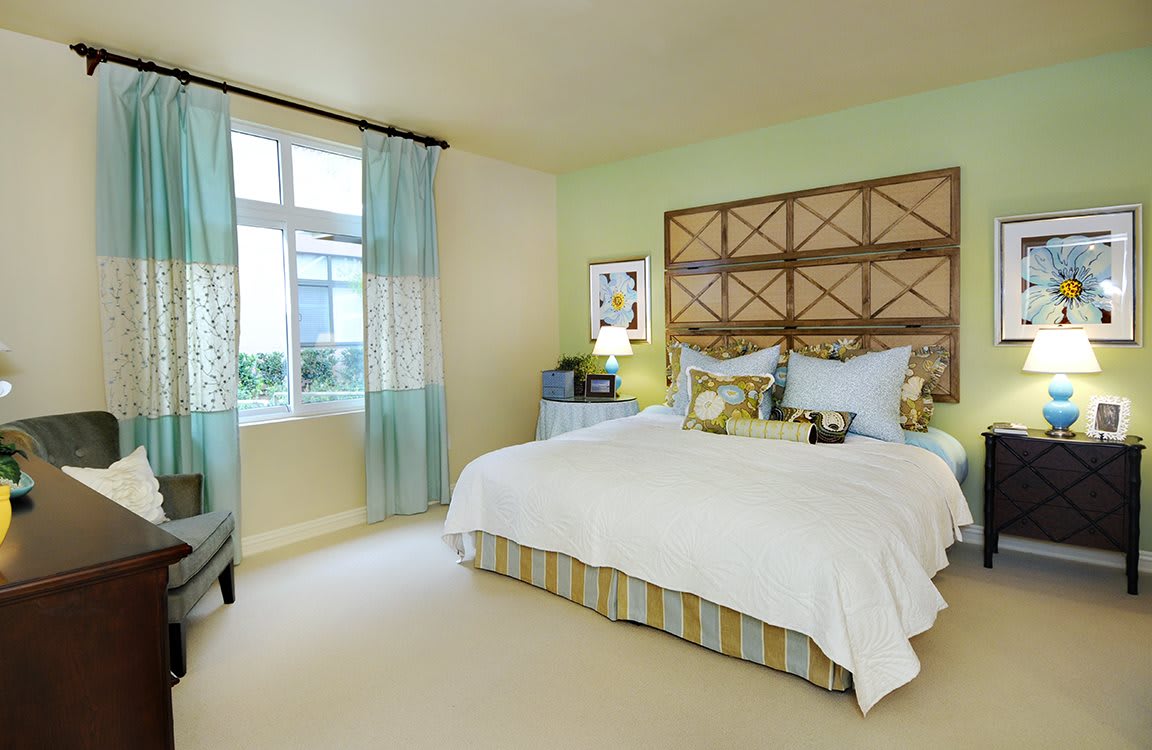 A cozy and well-decorated bedroom featuring a large bed with multiple pillows, soft lighting, and a window with light curtains.