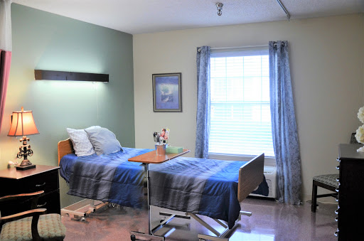 A well-lit patient room featuring two hospital beds, a window with blue curtains, and decorative artwork on the wall.