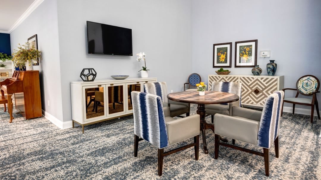A modern living room featuring a stylish dining area with a wooden table and mixed fabric chairs, complemented by wall art and a mounted television.
