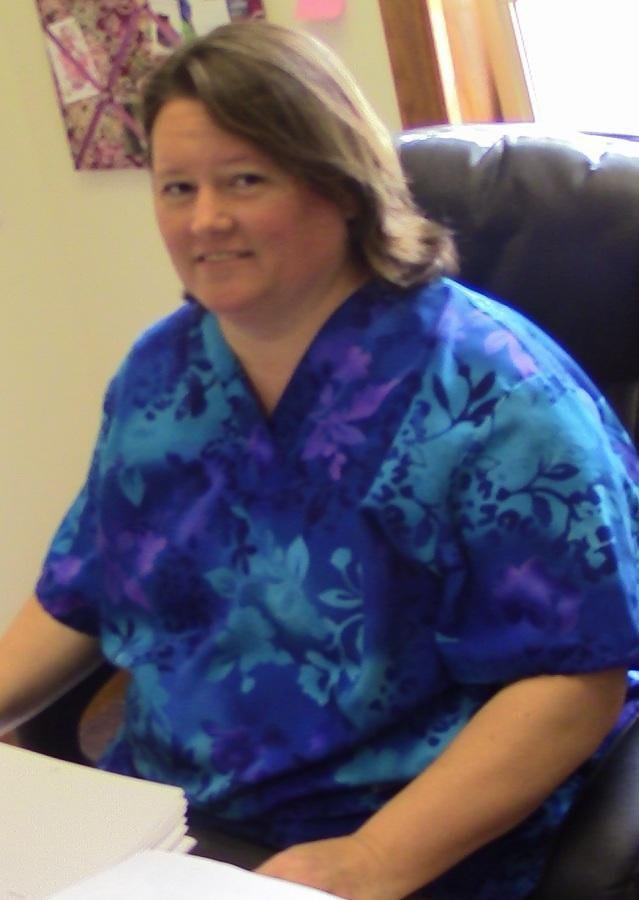 A person sitting in an office wearing a blue patterned shirt.