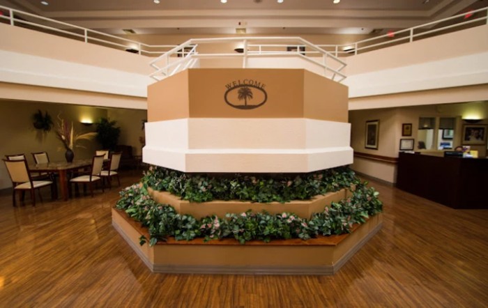 Hotel lobby area with decorative plants and a central structure featuring the hotel's logo.