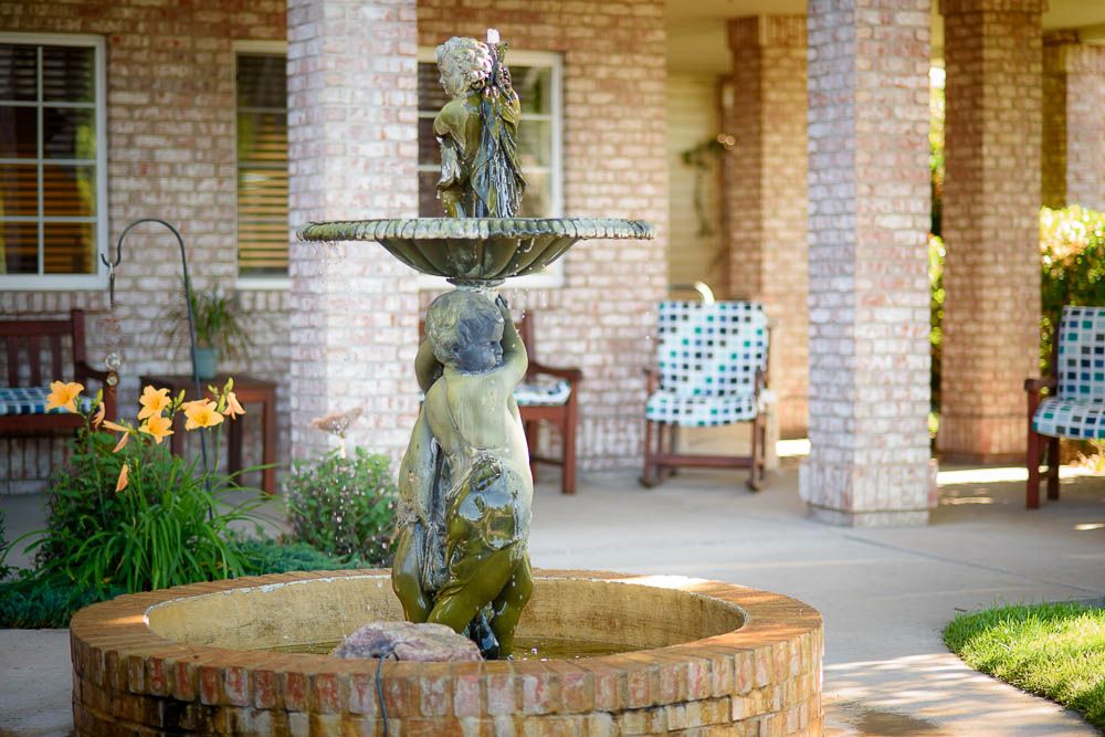 A decorative fountain in a patio area with brick walls and garden furniture.