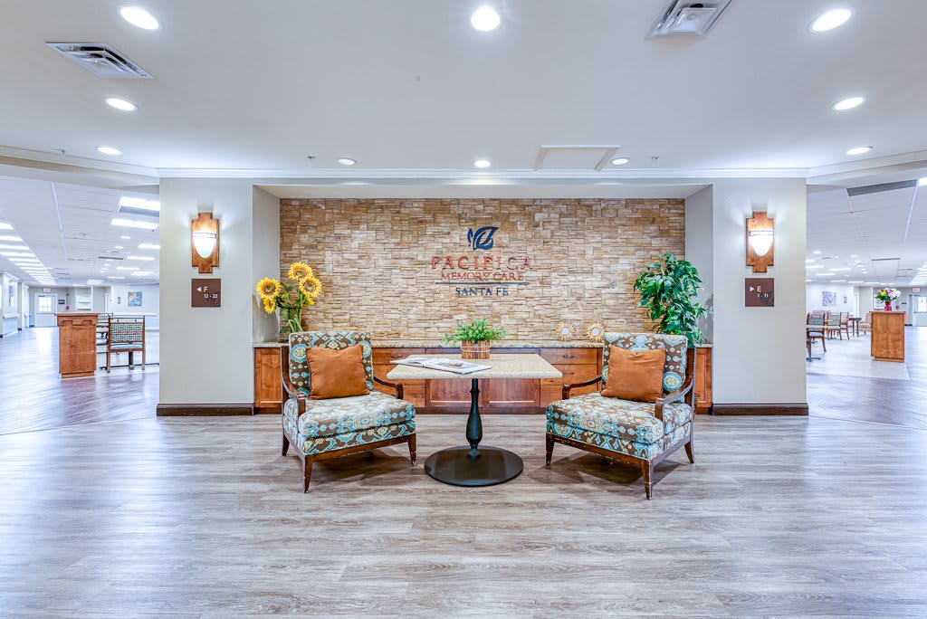 A cozy lobby area featuring two patterned chairs, a small table with decorative plants, and a brick wall backdrop.