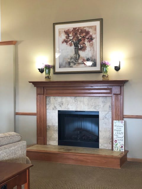 A cozy living room with a wooden fireplace mantel, adorned with a floral painting and wall sconces.