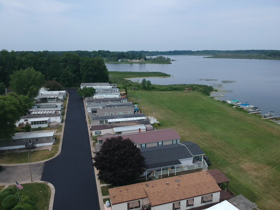 Aerial view of houses by a lake with a road and surrounding greenery.