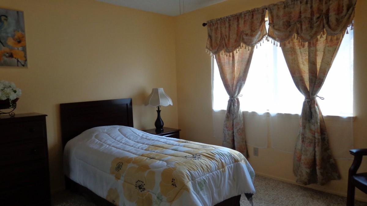 A cozy bedroom with a single bed, a lamp on the bedside table, and sunlight streaming through the window.